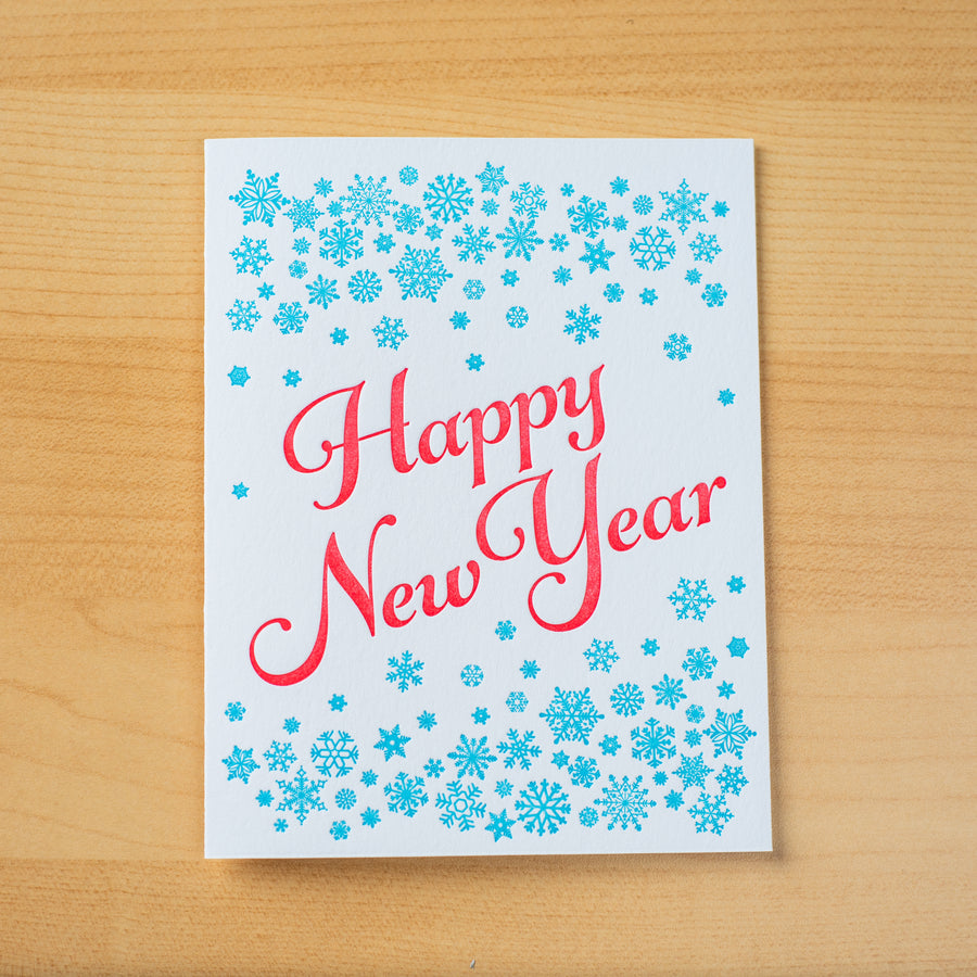 Letterpress greeting card with small turquoise snowflakes encircling the words Happy New Year