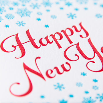 Letterpress greeting card with small turquoise snowflakes encircling the words Happy New Year