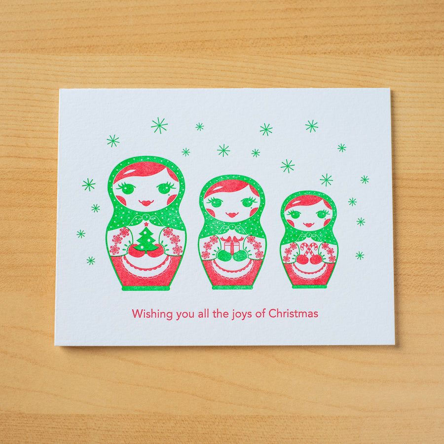 Letterpress Christmas greeting card of three nesting dolls holding gifts