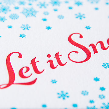 Letterpress holiday greeting card with small turquoise snowflakes encircling the phrase Let it Snow