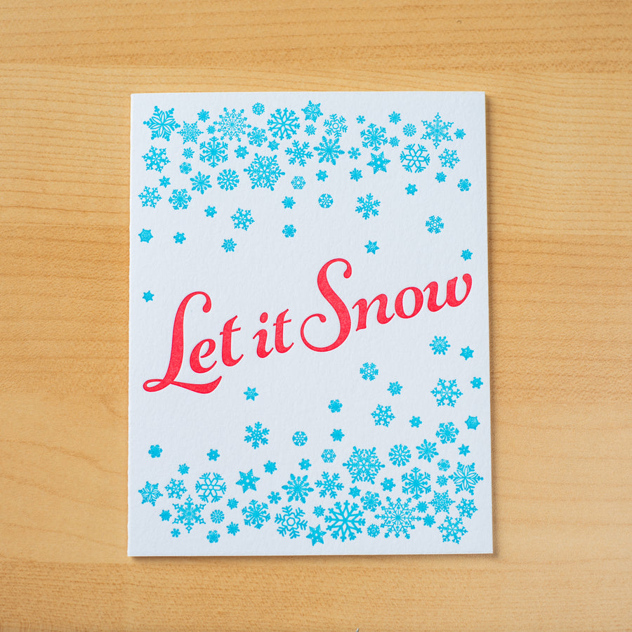 Letterpress holiday greeting card with small turquoise snowflakes encircling the phrase Let it Snow